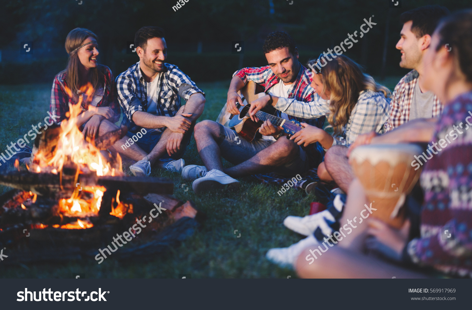 Happy friends playing music and enjoying bonfire in nature