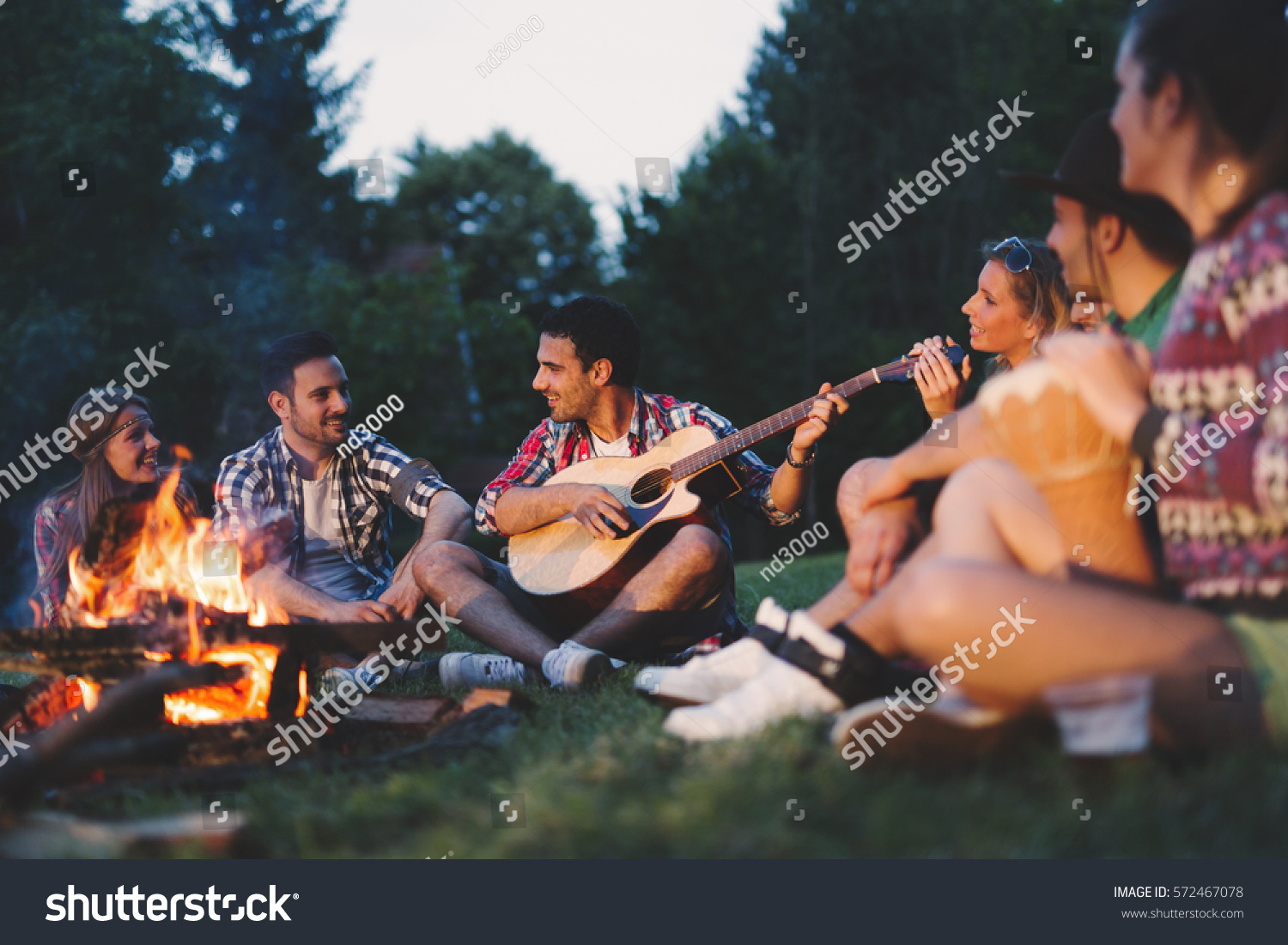 Happy friends playing music and enjoying bonfire in nature