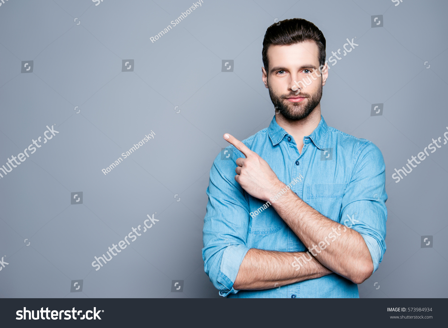 Handsome smiling bearded man pointing away on gray background.