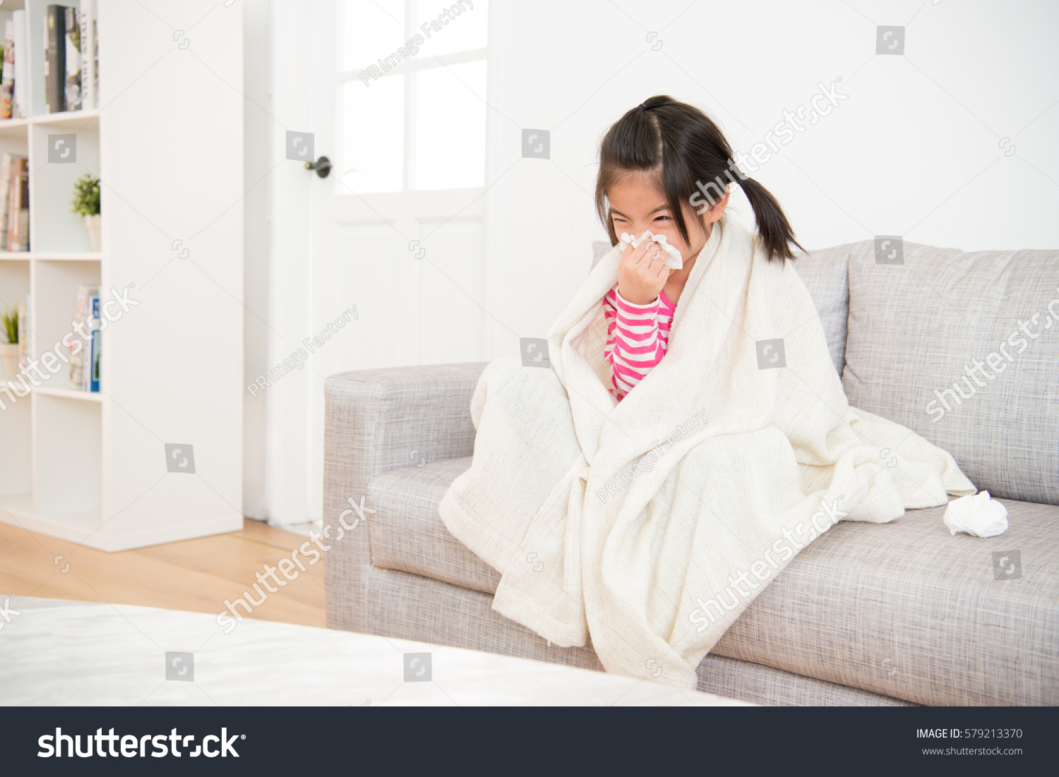 Little girl sick blowing her nose with tissue and cover with blanket sitting on sofa in the living room at home. family activity concept.