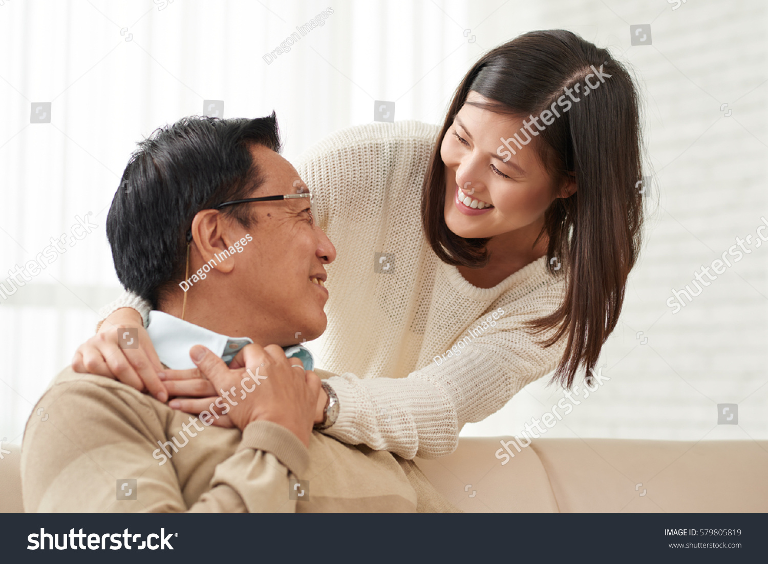 Lovely family moments: Asian young woman standing behind her senior dad and hugging him tenderly he turned to her and smiling