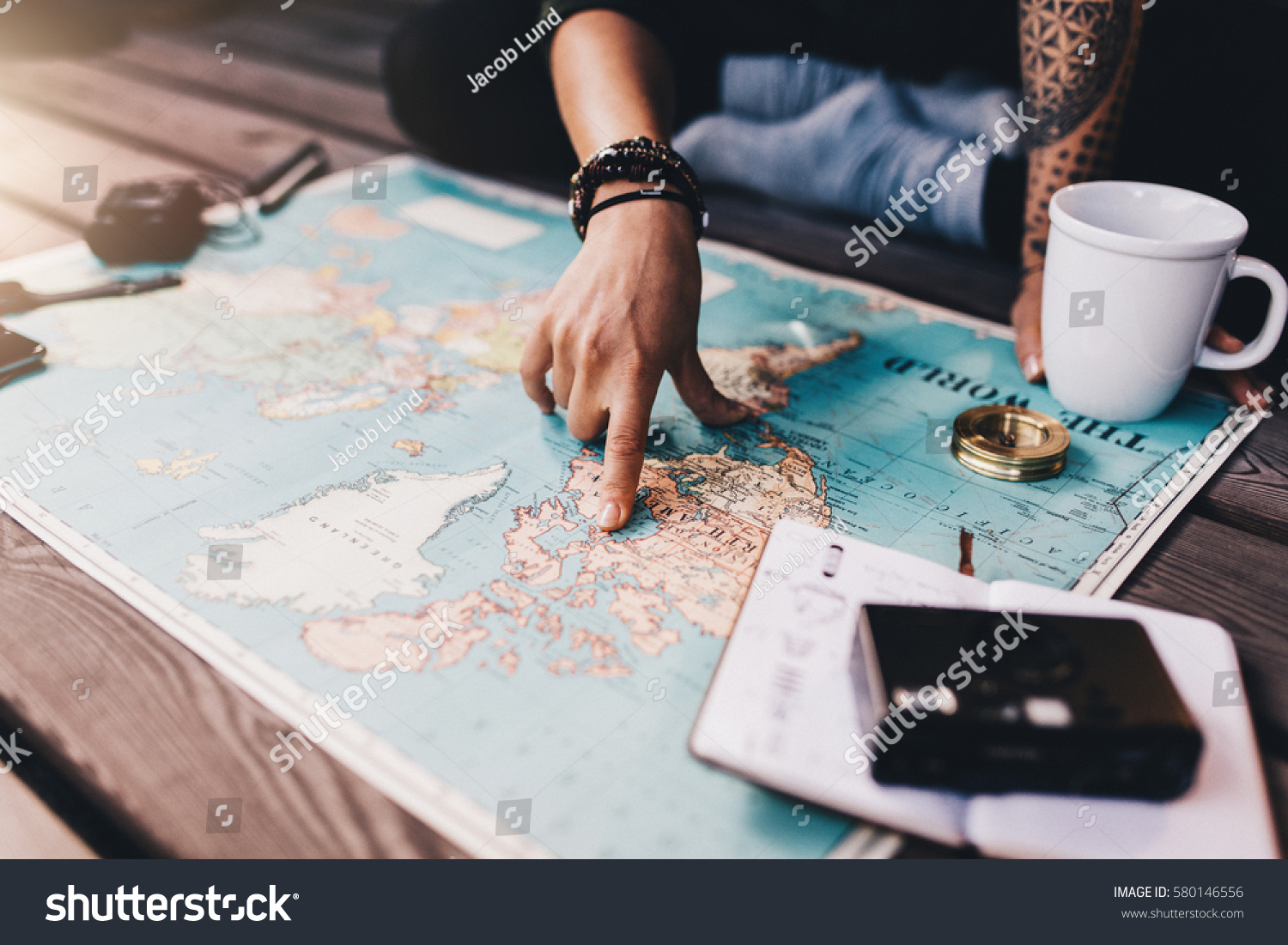 Tourist planning vacation with the help of world map with other travel accessories around. Young woman pointing at North America on the world map.