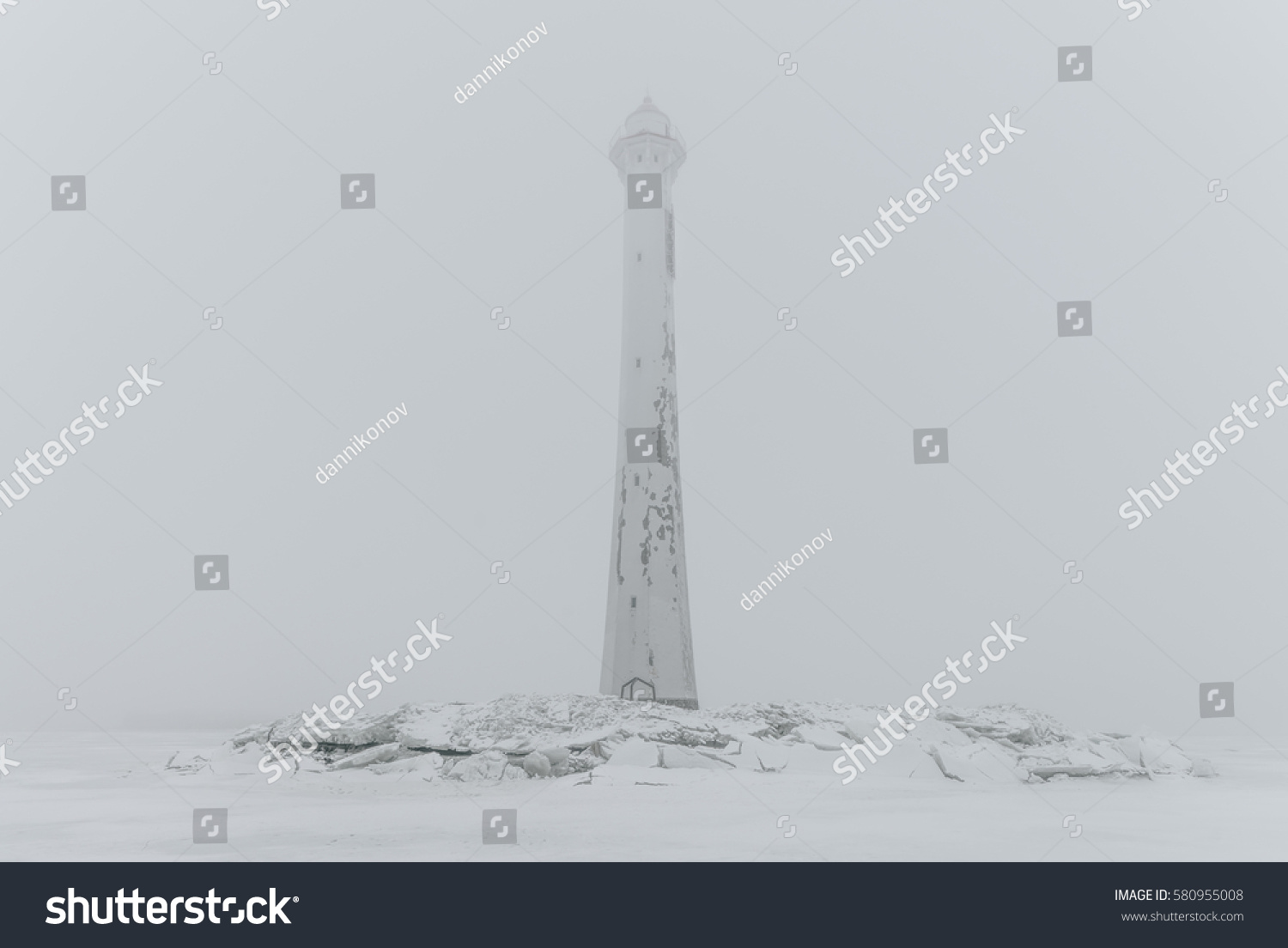 Foggy lighthouse in a calm and desolate winter landscape. A white old lighthouse isolated in mist.