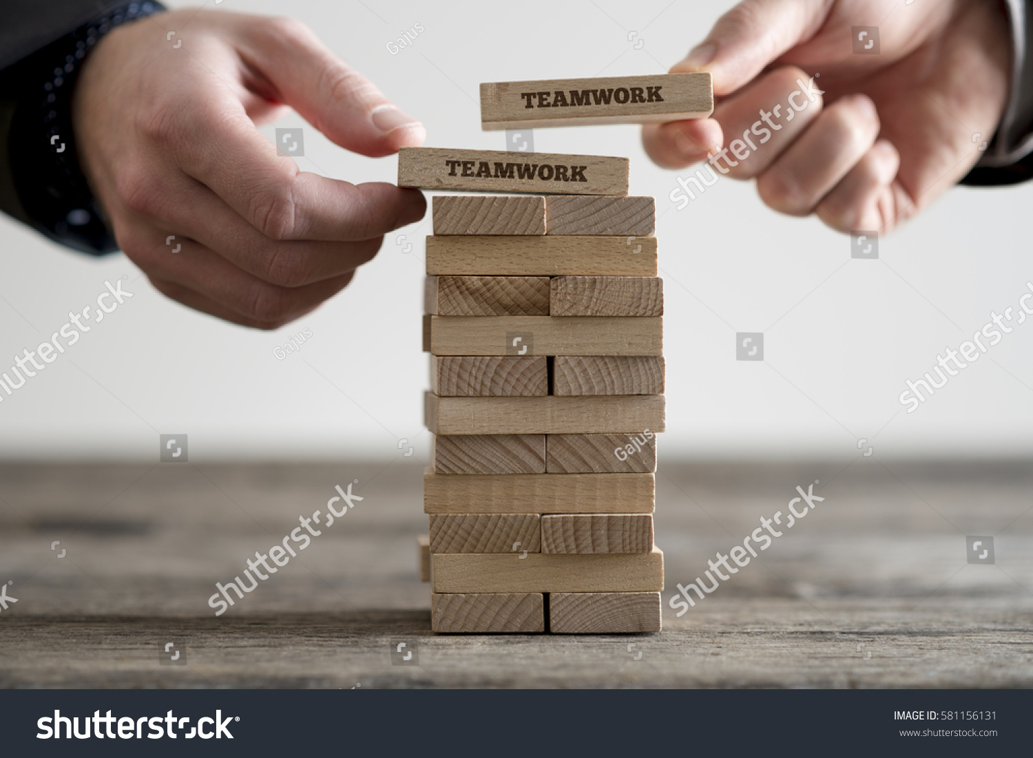 Two hands putting dominoes onto stack of wooden bricks with teamwork business signs on rustic table surface.
