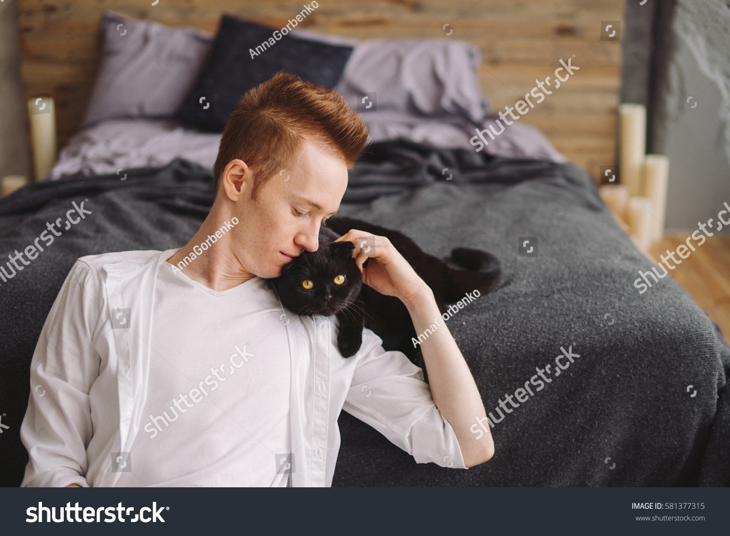 Happy young handsome caucasian man sitting with a black cat. Playing with pet at home. Love coziness leisure animal protection concept. Scottish fold breed.
