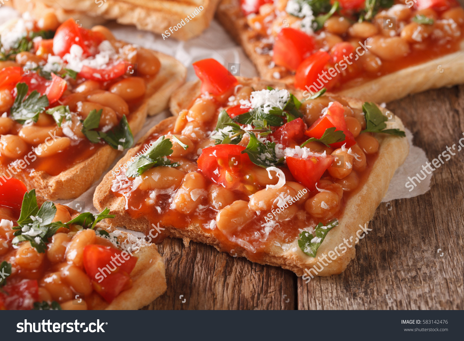 toasts with beans in a tomato sauce  cheese and herbs closeup on the table. Horizontal
