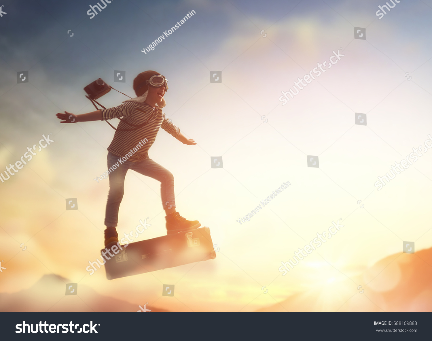 Dreams of travel! Child flying on a suitcase against the backdrop of sunset.