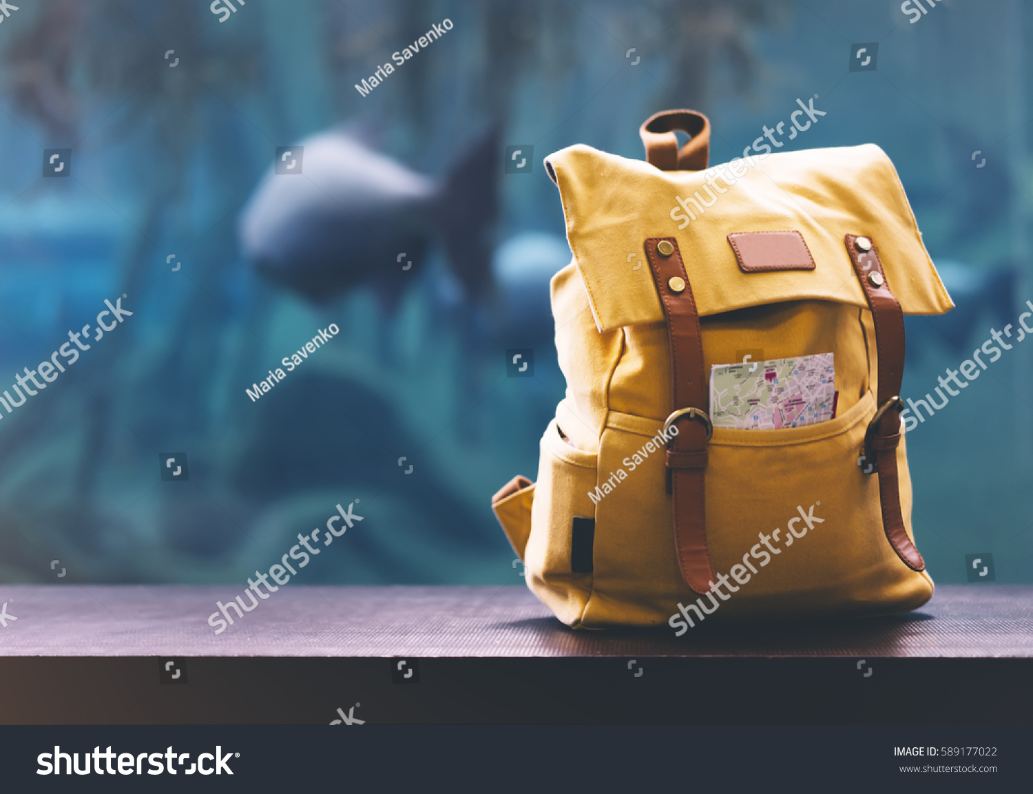 Hipster yellow backpack and map closeup. View from front tourist traveler bag on background blue sea aquarium. Person hiker visiting ocean museum in Barcelona on backdrop  blank blurred mock up