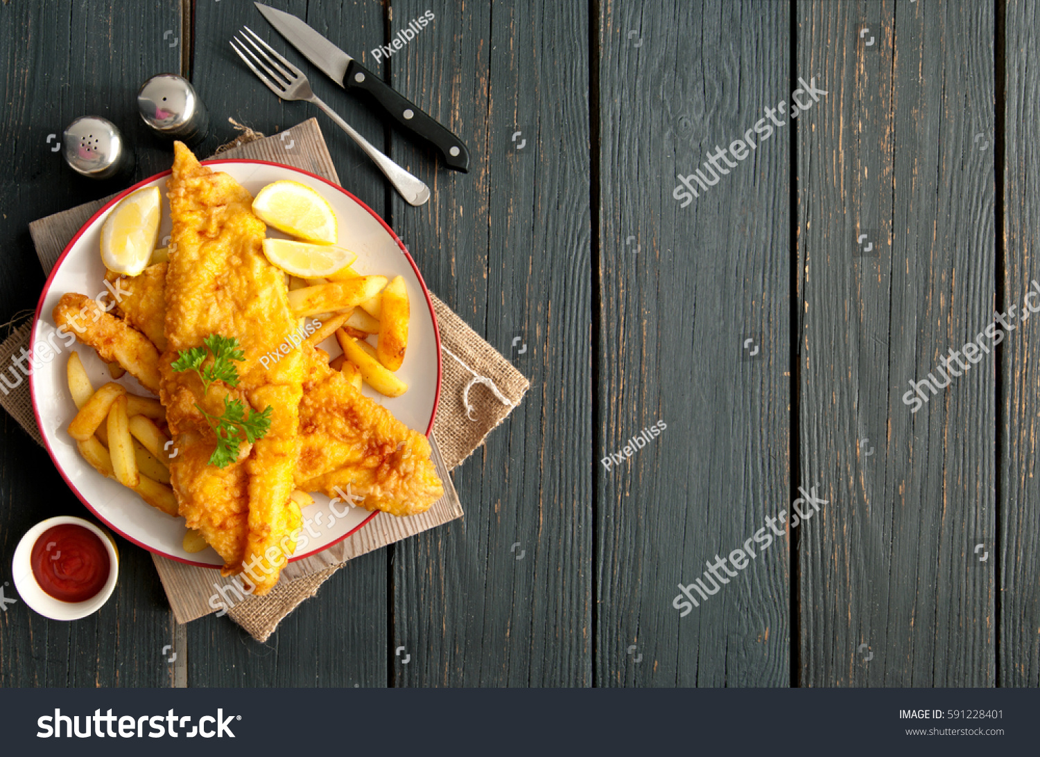 Two pieces of battered fish on a plate with chips on a wooden table with space 