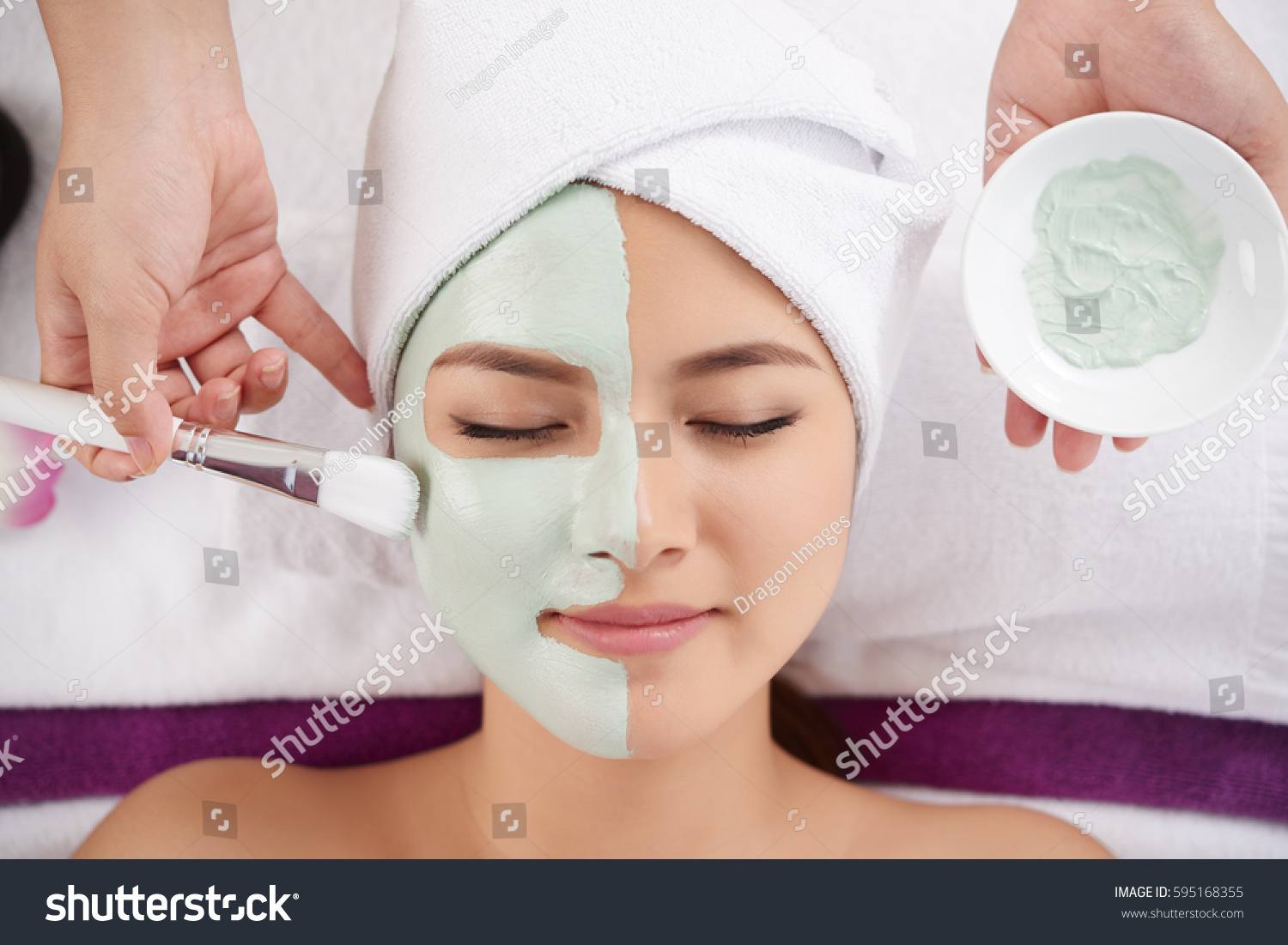 Beautician applying clay face mask on face of pretty woman