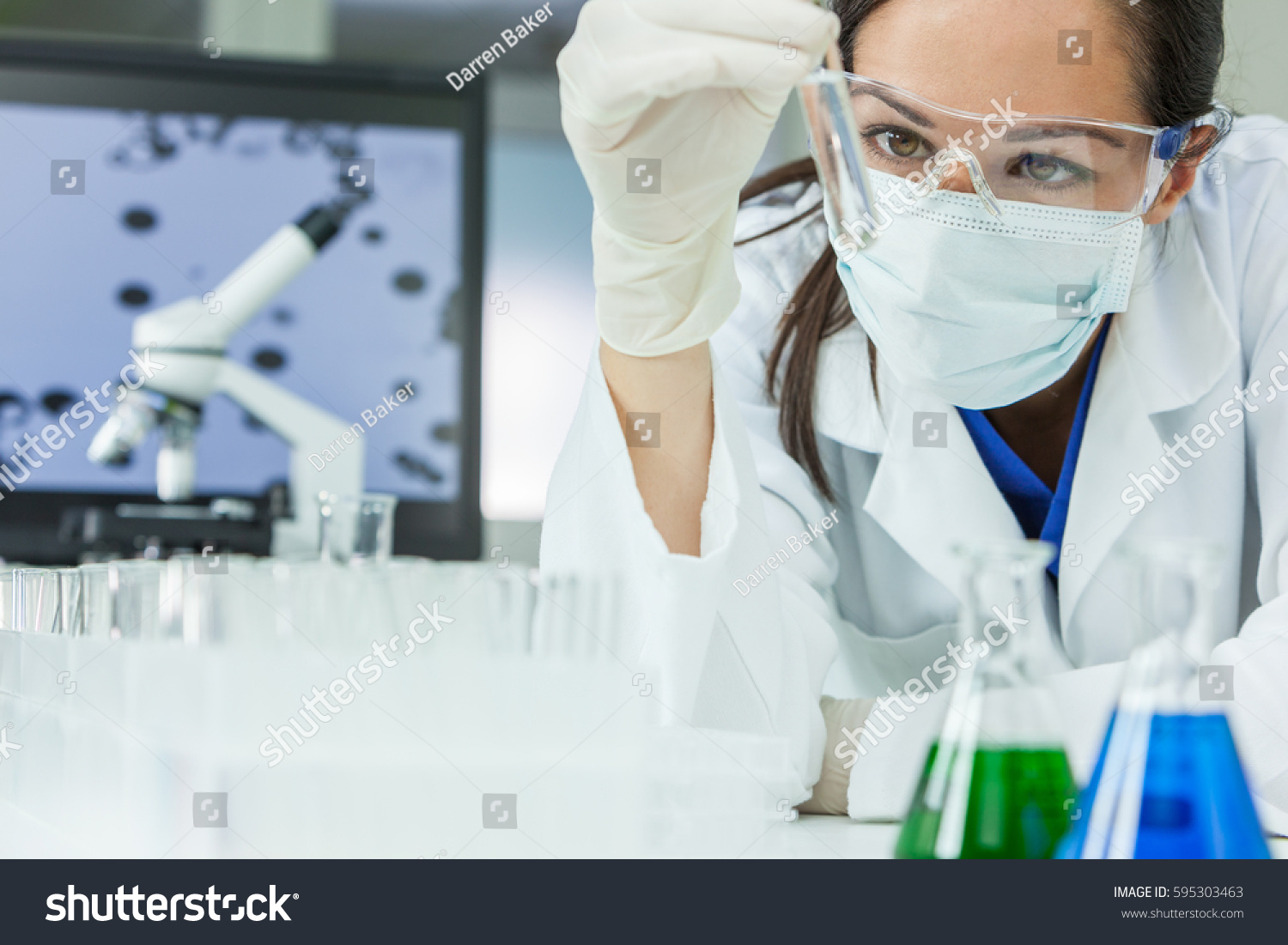 Female medical or research scientist or doctor using looking at a test tube of clear solution in a lab or laboratory