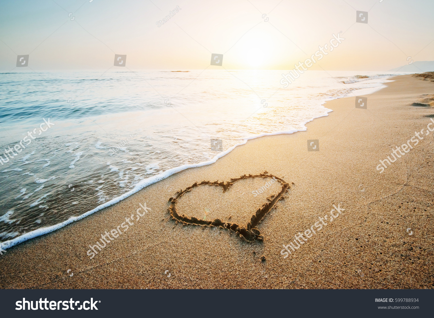 Drawing heart on yellow sand on the fantastic sunset.