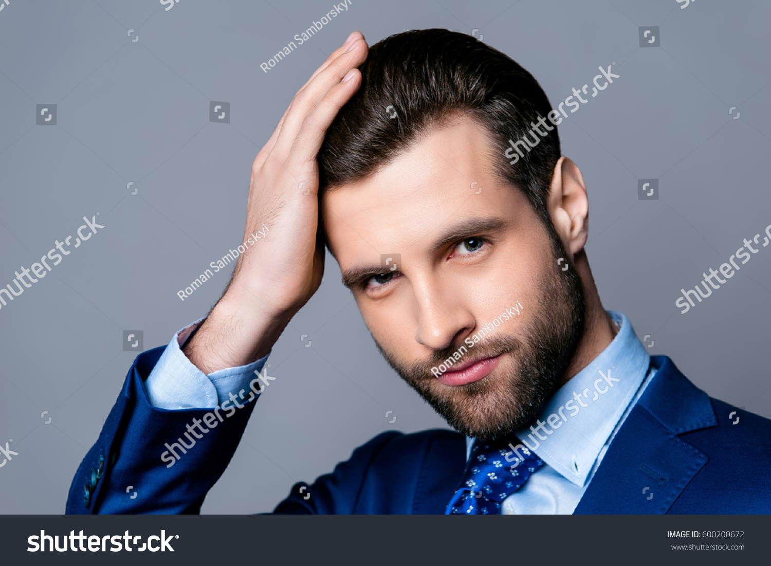 Close up portrait of serious handsome man in blue suit and tie touching his perfect hair