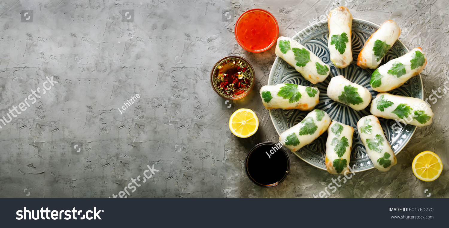 Fresh Vietnamese Asian Chinese food frame on grey concrete background. Spring rolls rice paper lettuce salad vermicelli noodles shrimps fish sauce sweet chili soy lemon. Top view