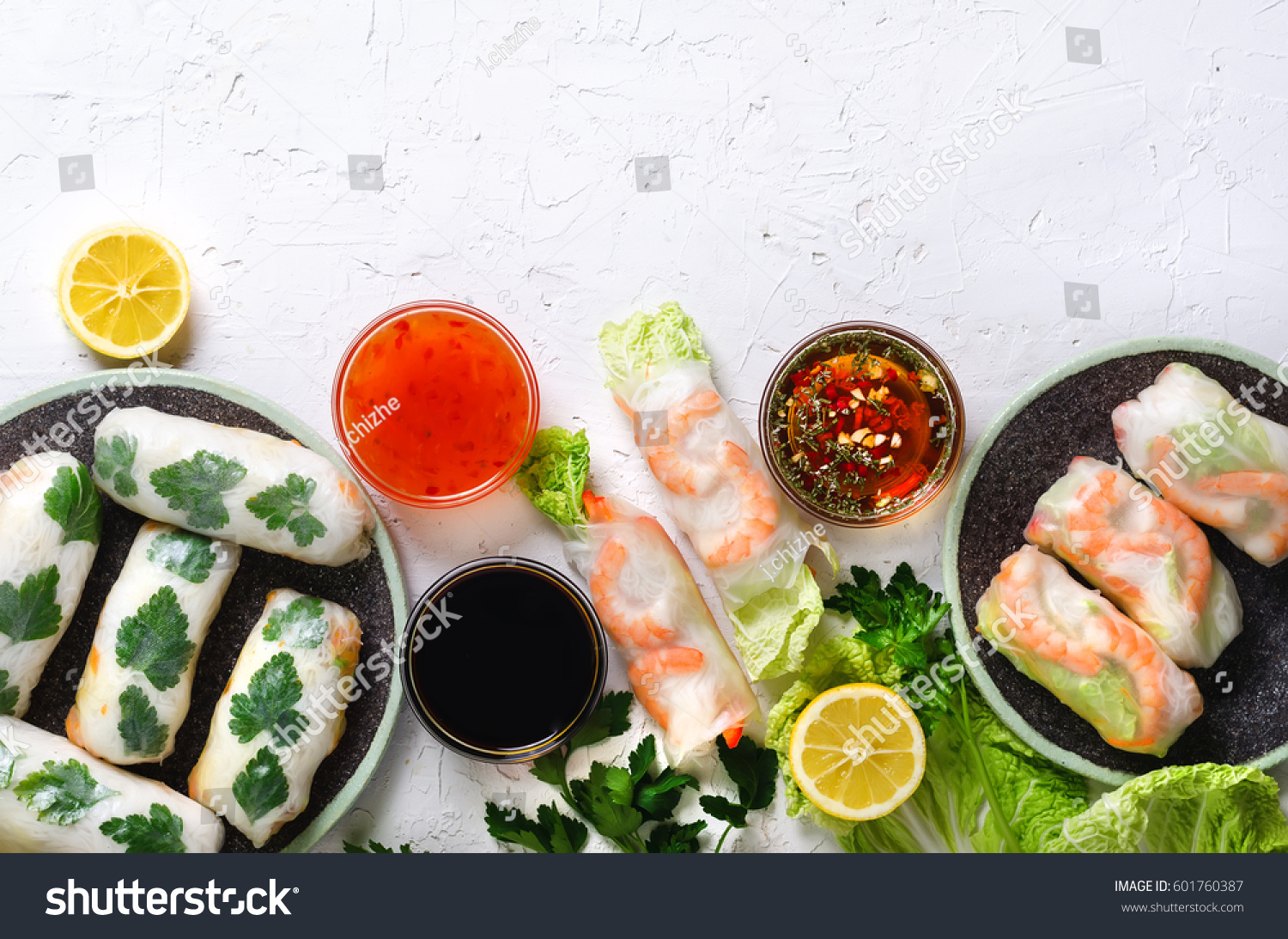Fresh Vietnamese Asian Chinese food frame on white concrete background. Spring rolls rice paper lettuce salad vermicelli noodles shrimps fish sauce sweet chili soy lemon. Top view.