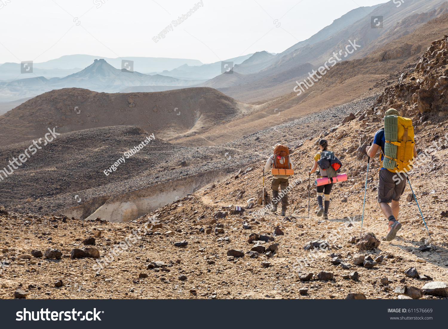Three backpackers tourists group walking hiking rocks desert path trail marking sign purple trailblazing marker    Ramon crater valley  Israel tourism traveling.