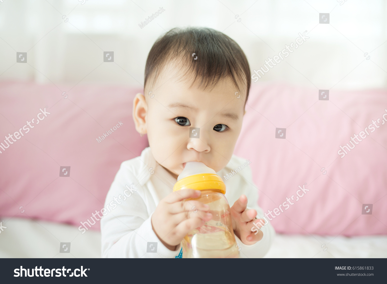 Sweet baby girl sucking milk in bottle at home.
