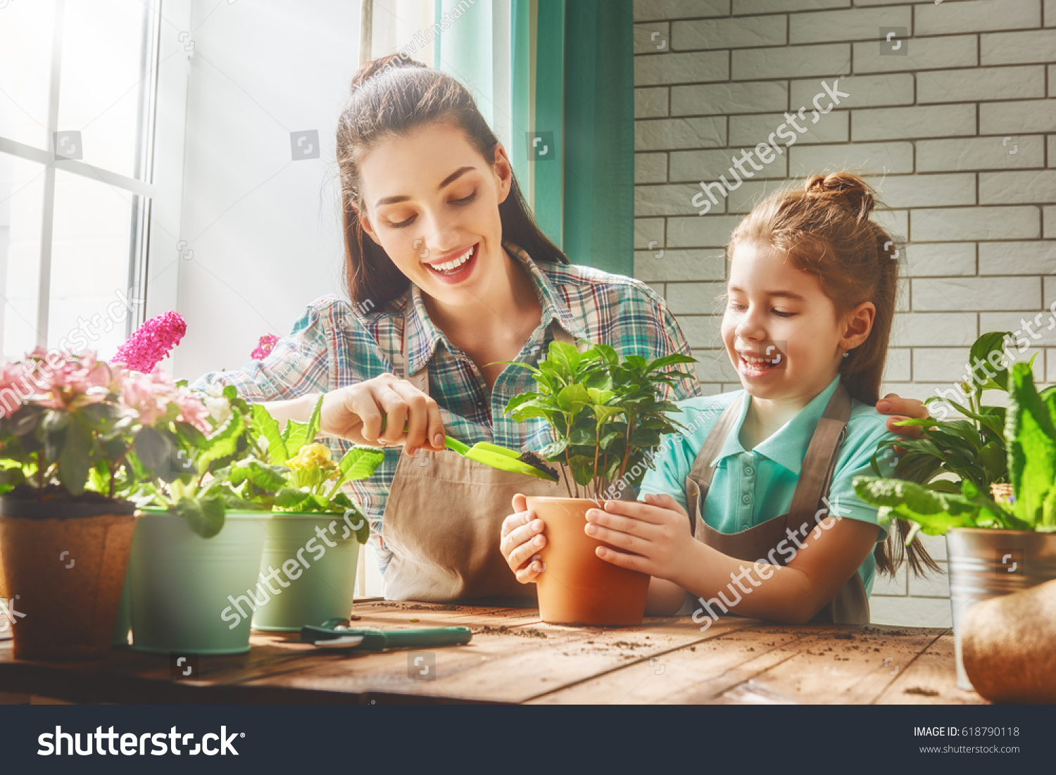 Cute child girl helps her mother to care for plants. Mom and her daughter engaged in gardening near window at home. Happy family in spring day.