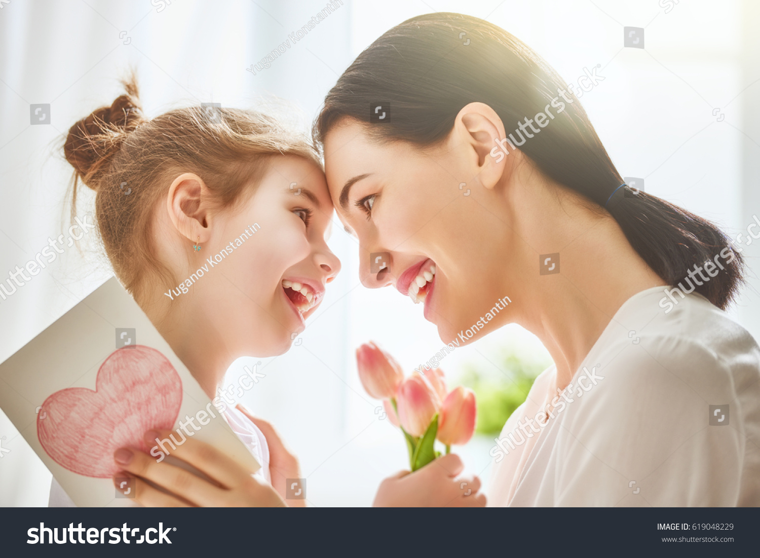 母亲节快乐！儿童女儿祝贺妈妈 并给她的鲜花郁金香和明信片。妈妈和女孩微笑着拥抱。家庭假期和团结。