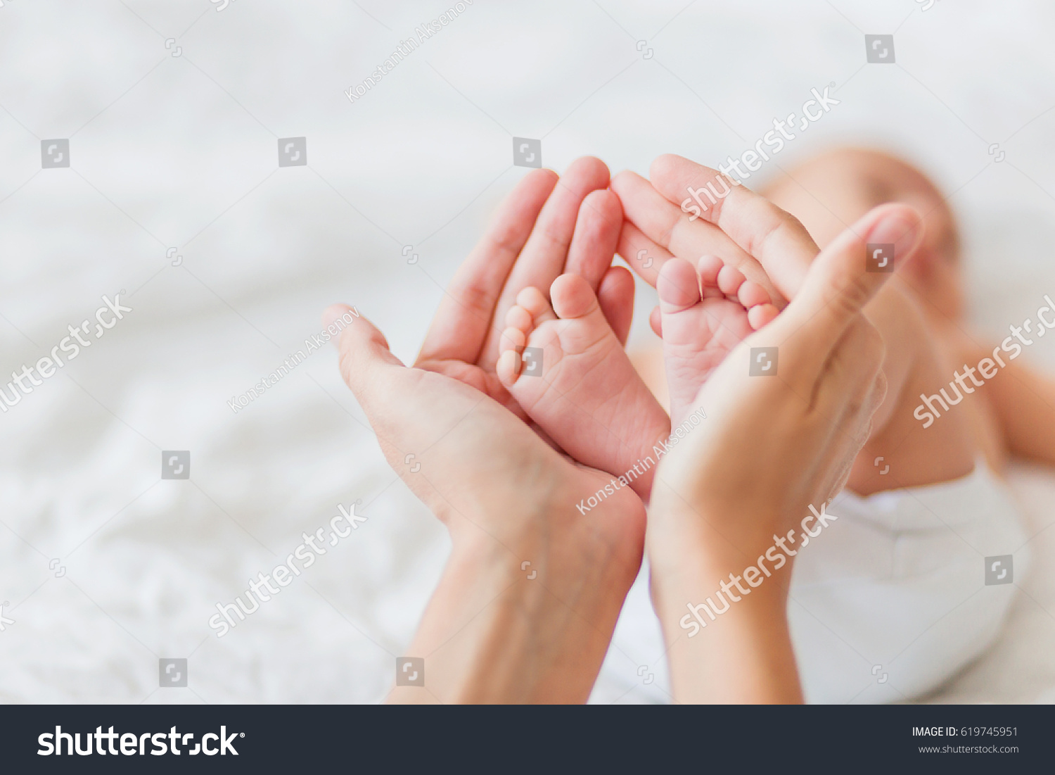 Mother holds newborn baby's bare feet. Tiny feet in woman's hand. Cozy morning at home.