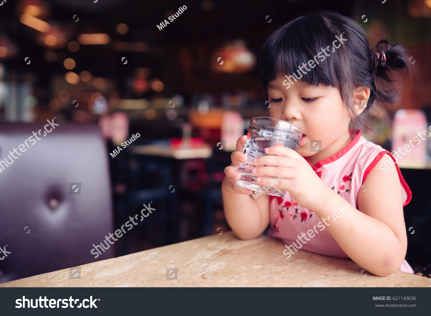 Happy adorable little girl drinking water.Smiling asian kid holding transparent glass in her hand.