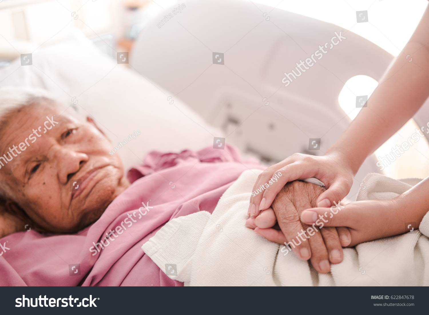 Caring hands holding old lady's hands in bed at hospital