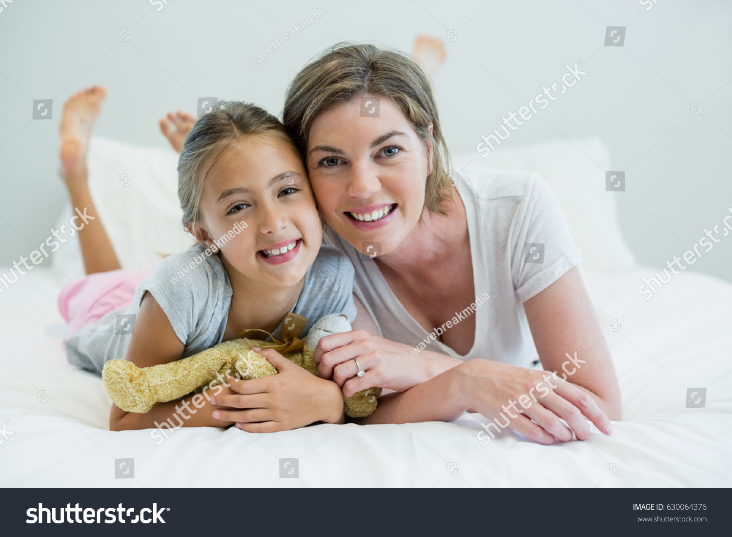 Portrait of smiling mother and daughter lying on bed in bedroom at home