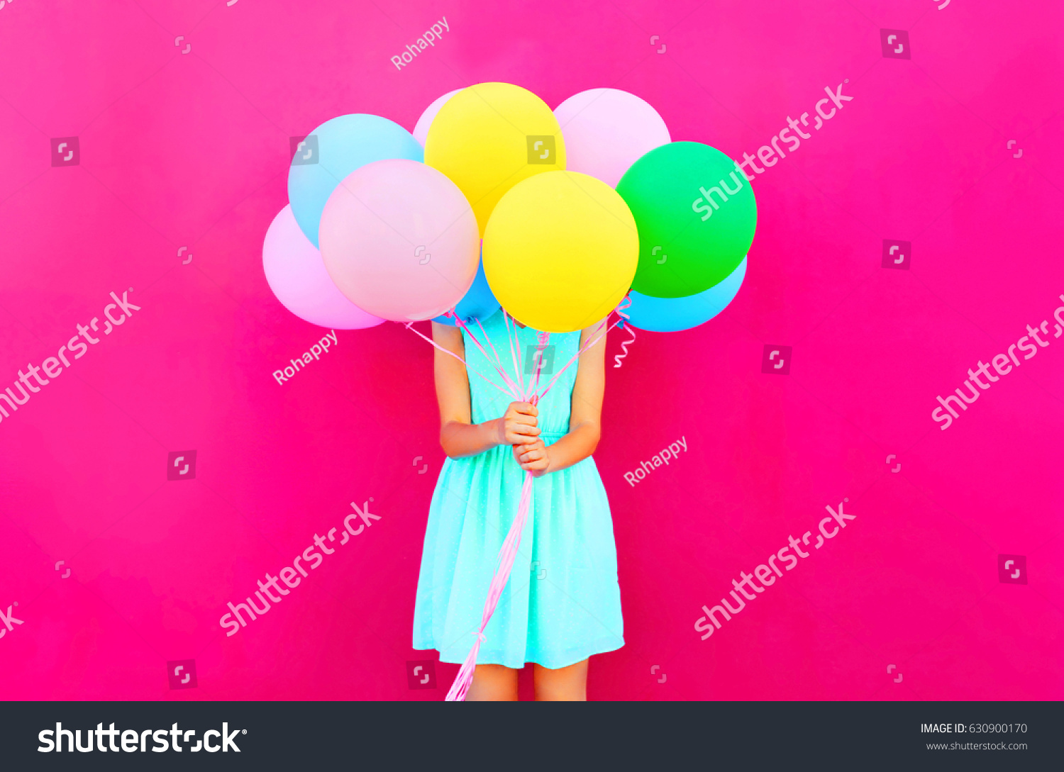 Woman is hides her head an air colorful balloons having fun over pink background