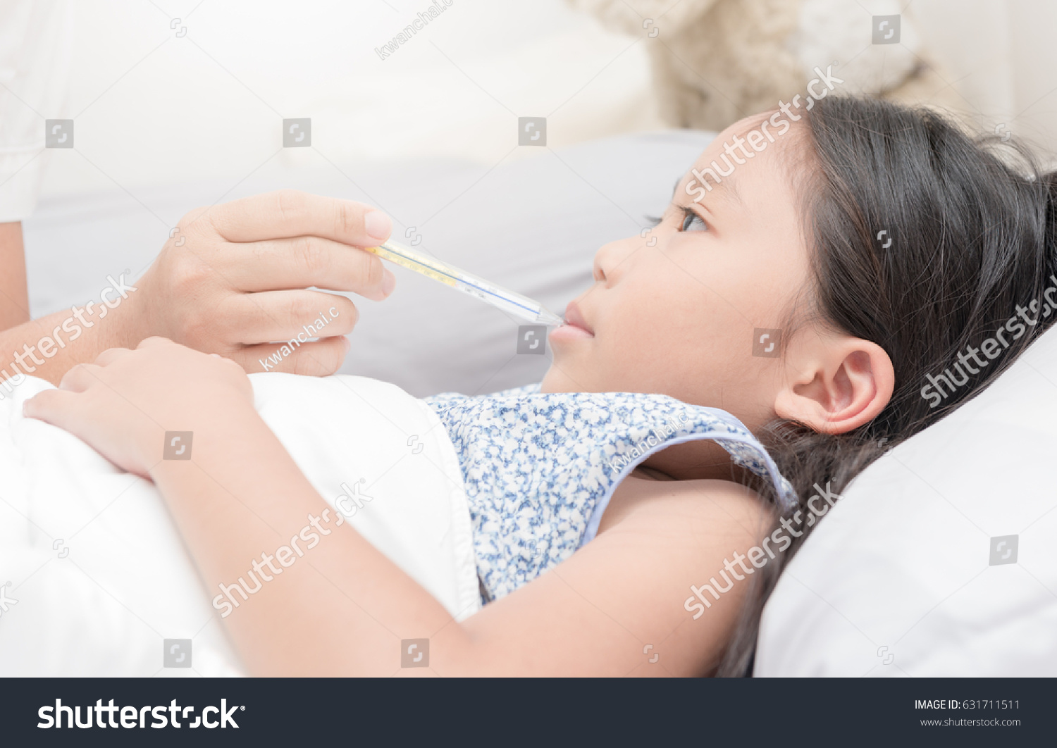 Mother measuring temperature of her ill kid. Sick child with high fever laying in bed and mother holding thermometer.focus on hand mother