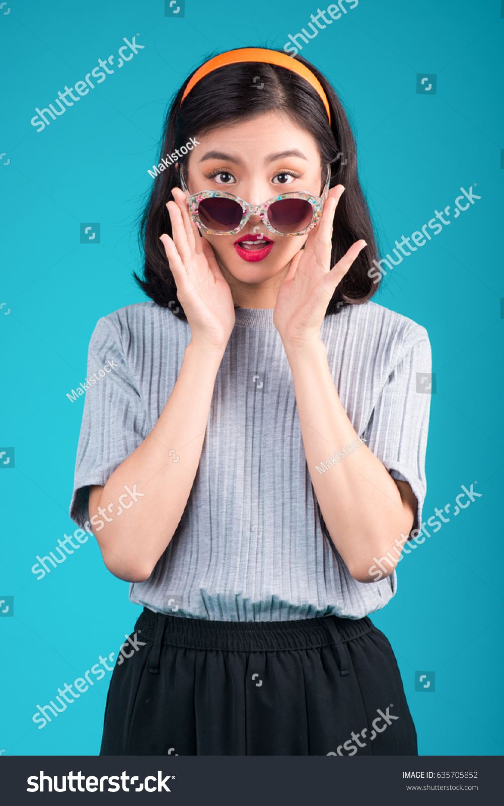 Smiling asian woman dressed in pin-up style dress wearing eyeglasses over blue.