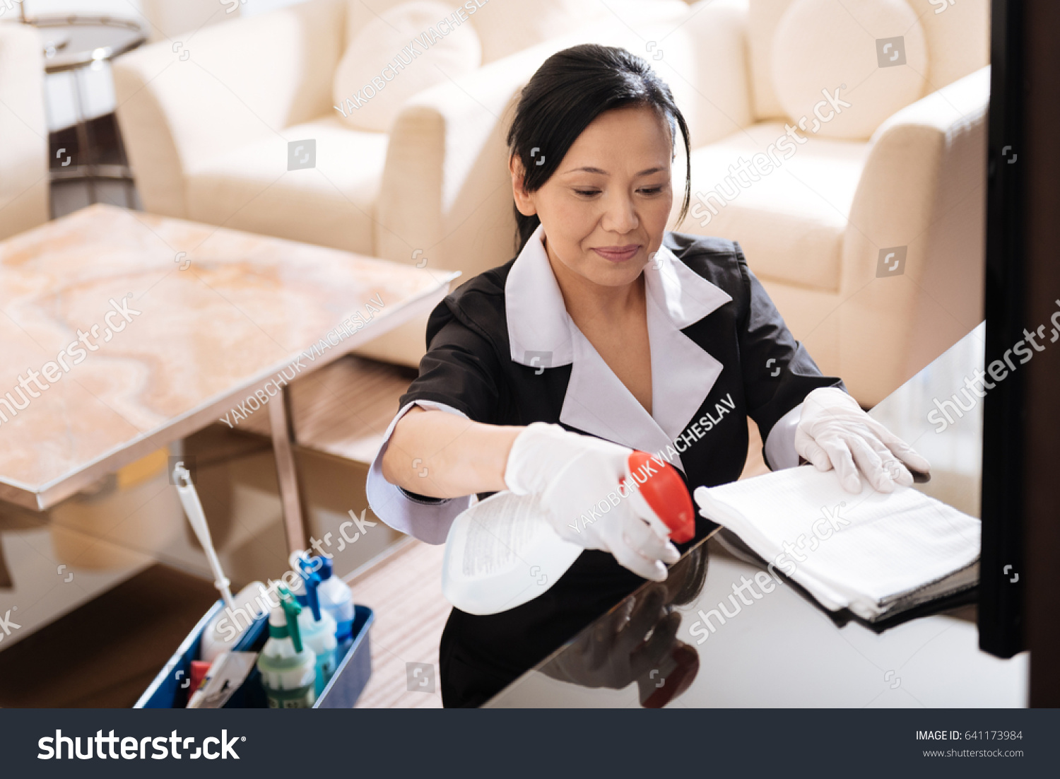 Nice pleasant woman spraying cleaning agent on the table
