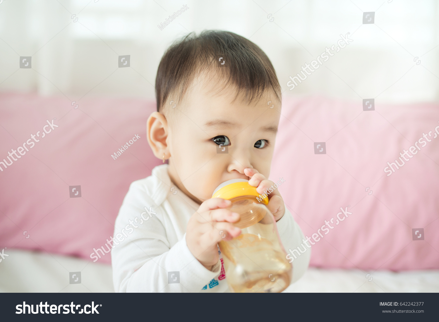 Sweet baby girl sucking milk in bottle at home.