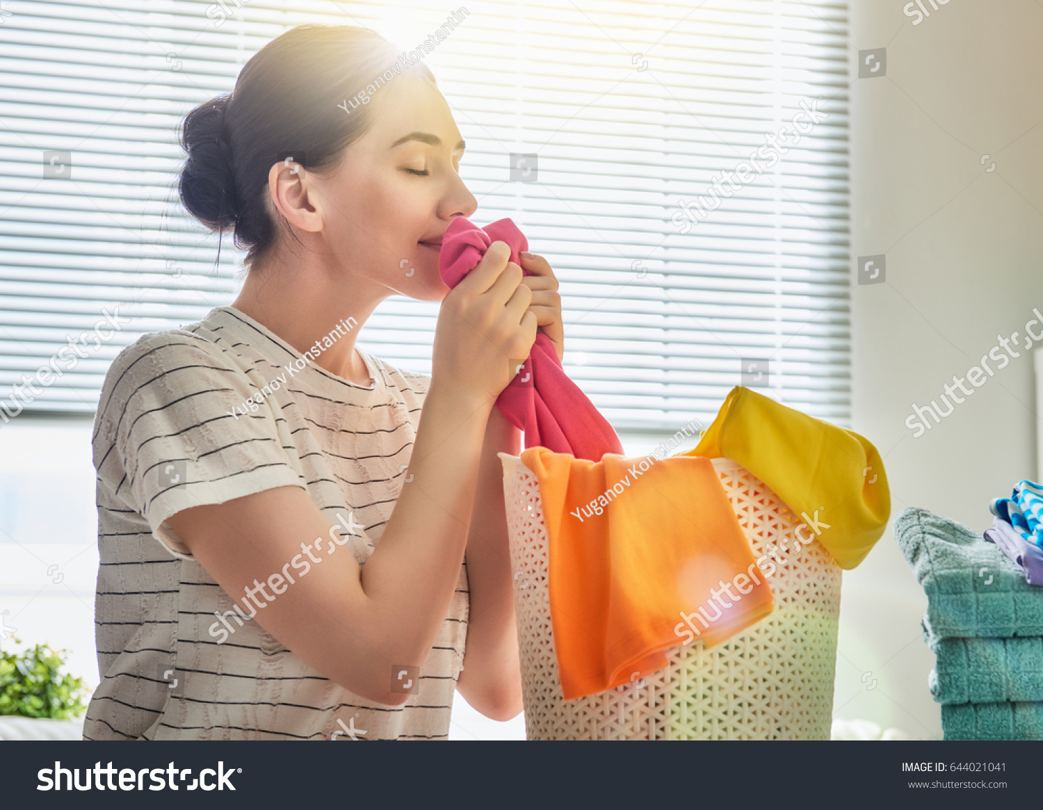 Beautiful young woman is smelling clean clothes and smiling while doing laundry at home.