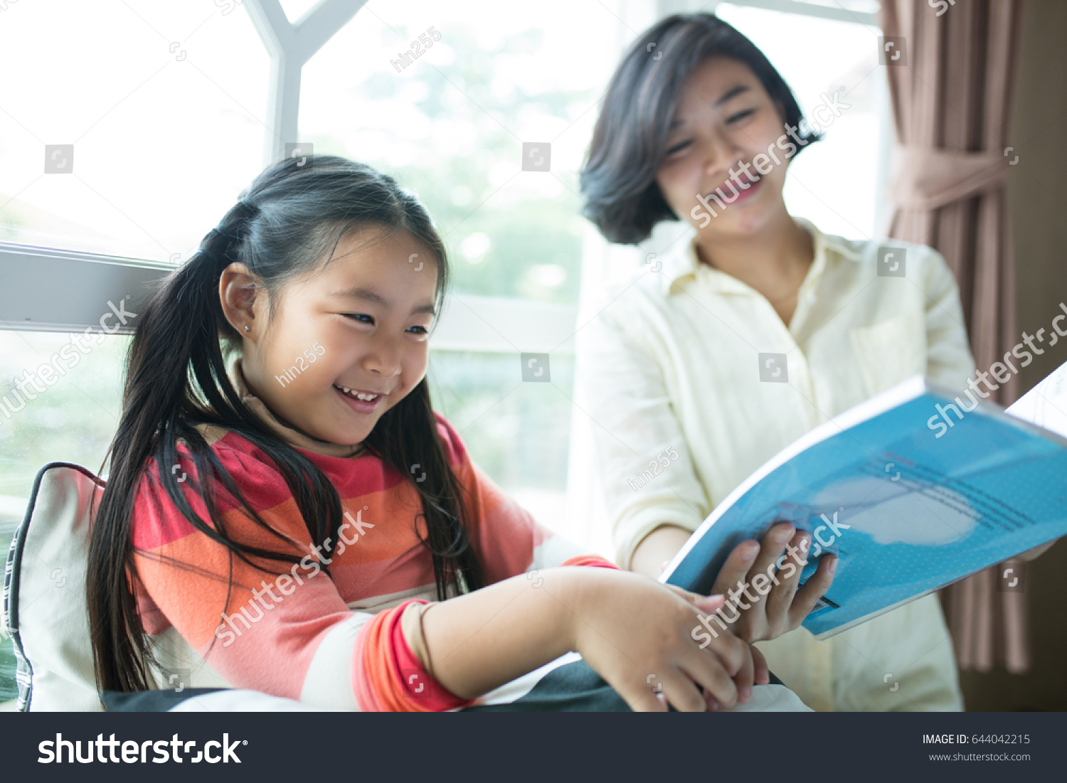 Asian Children reading book with her mother in living room.
