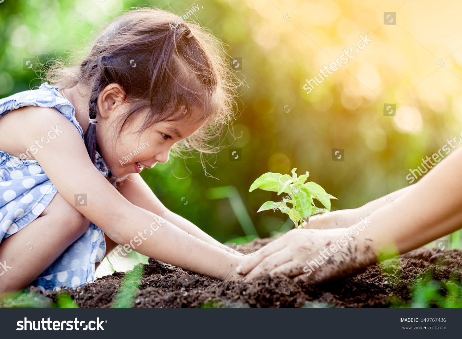 Asian little girl and parent planting young tree on black soil together as save world concept in vintage color tone