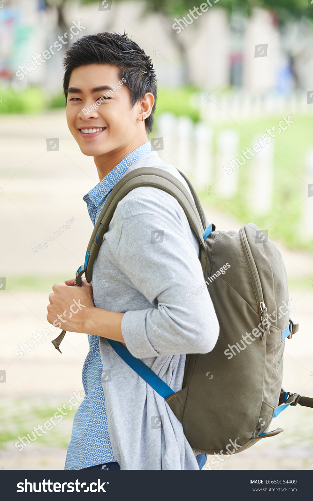 Handsome college student with backpack standing in profile and looking at camera with toothy smile waist-up portrait