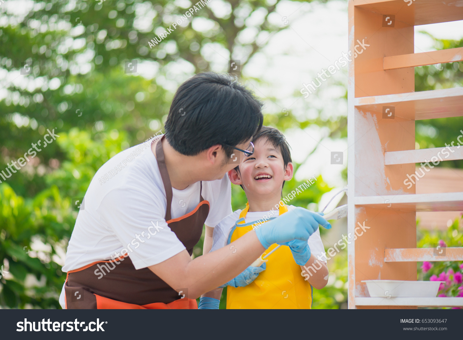 Asian father and son painting wooden shelf together