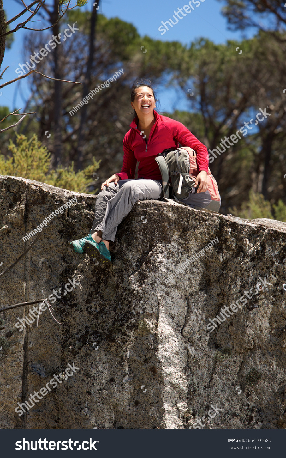 Portrait of cheerful asian female hiker sitting at the edge of mountain and laughing
