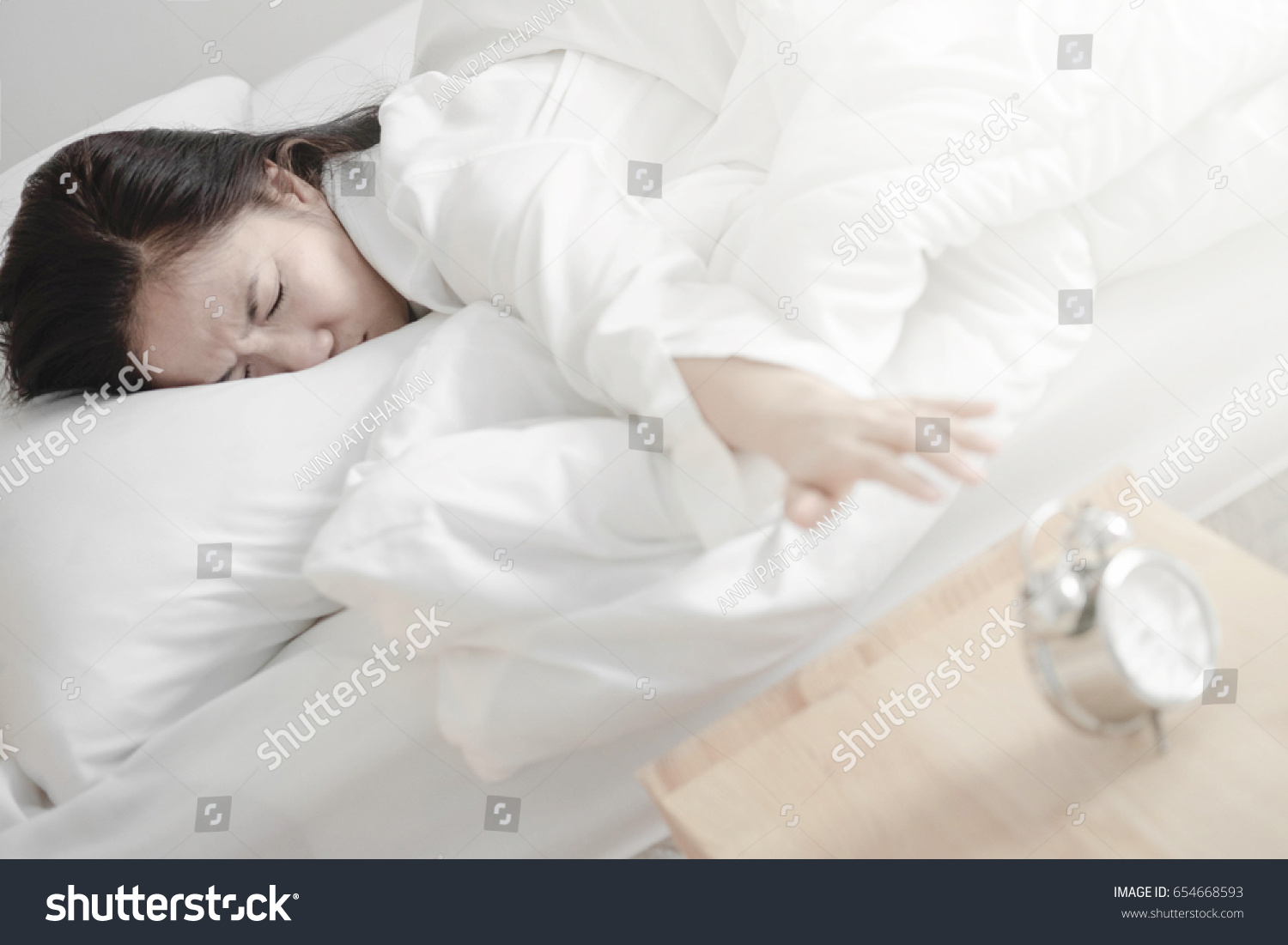Asian girl Trying to get up from bed in the morning. Reach for bedside alarm clock.