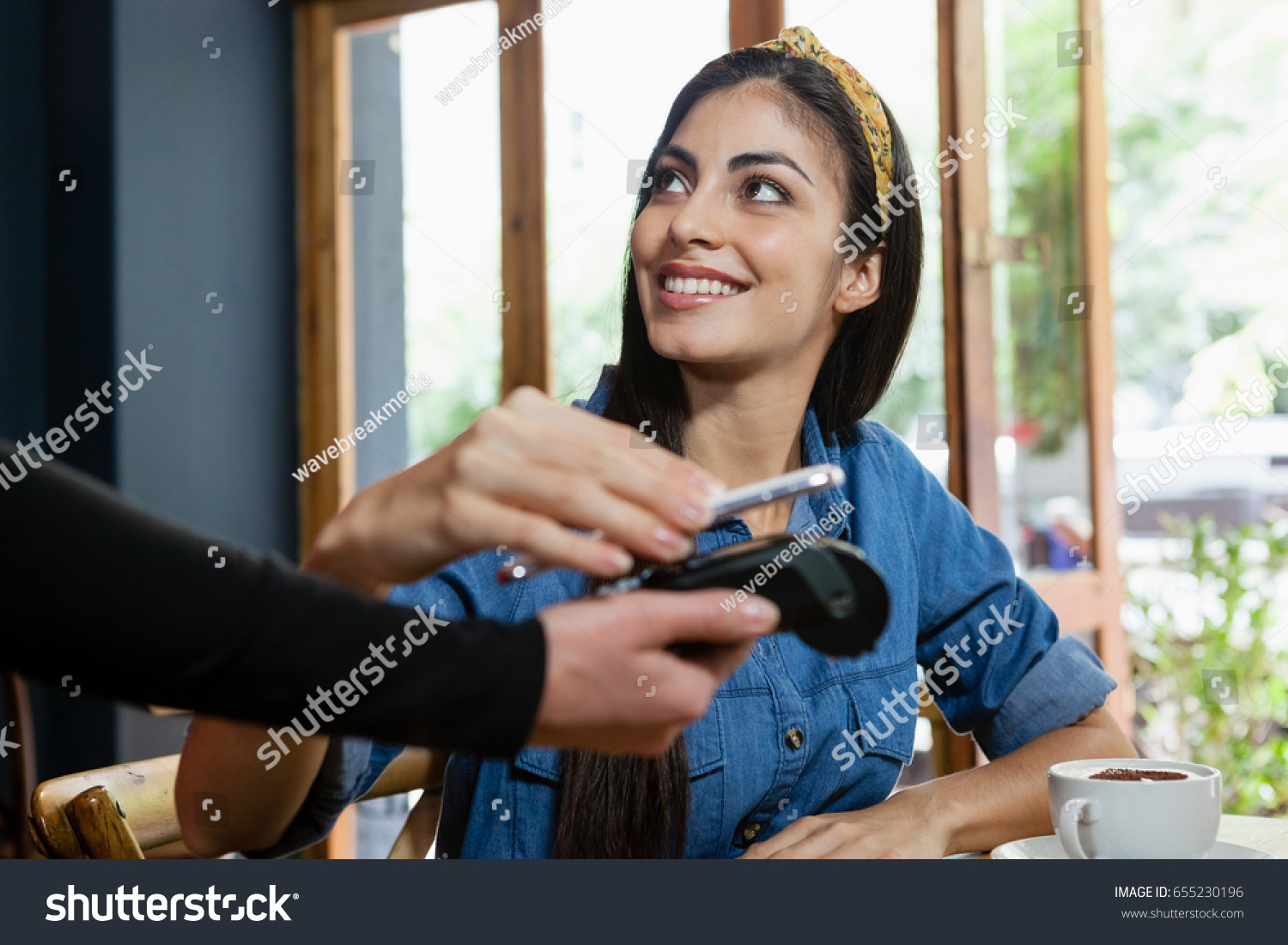 Smiling woman making payment on credit card reader at cafe shop