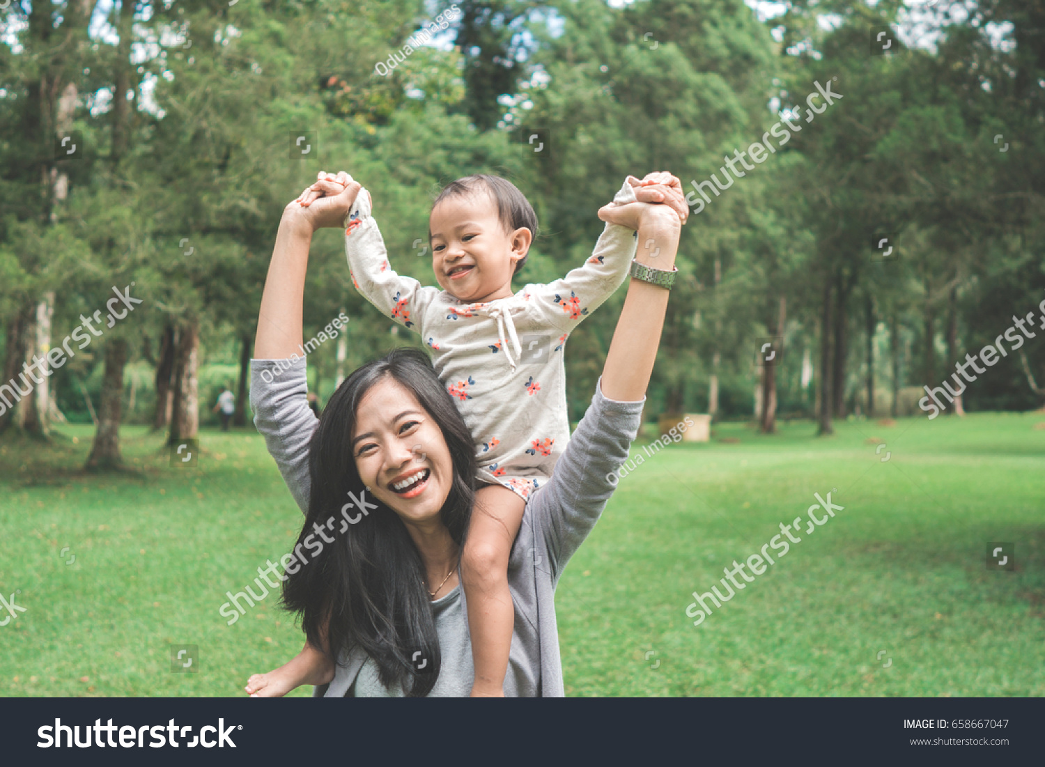 portrait of happy baby girl sitting on mom's shoulder in the park