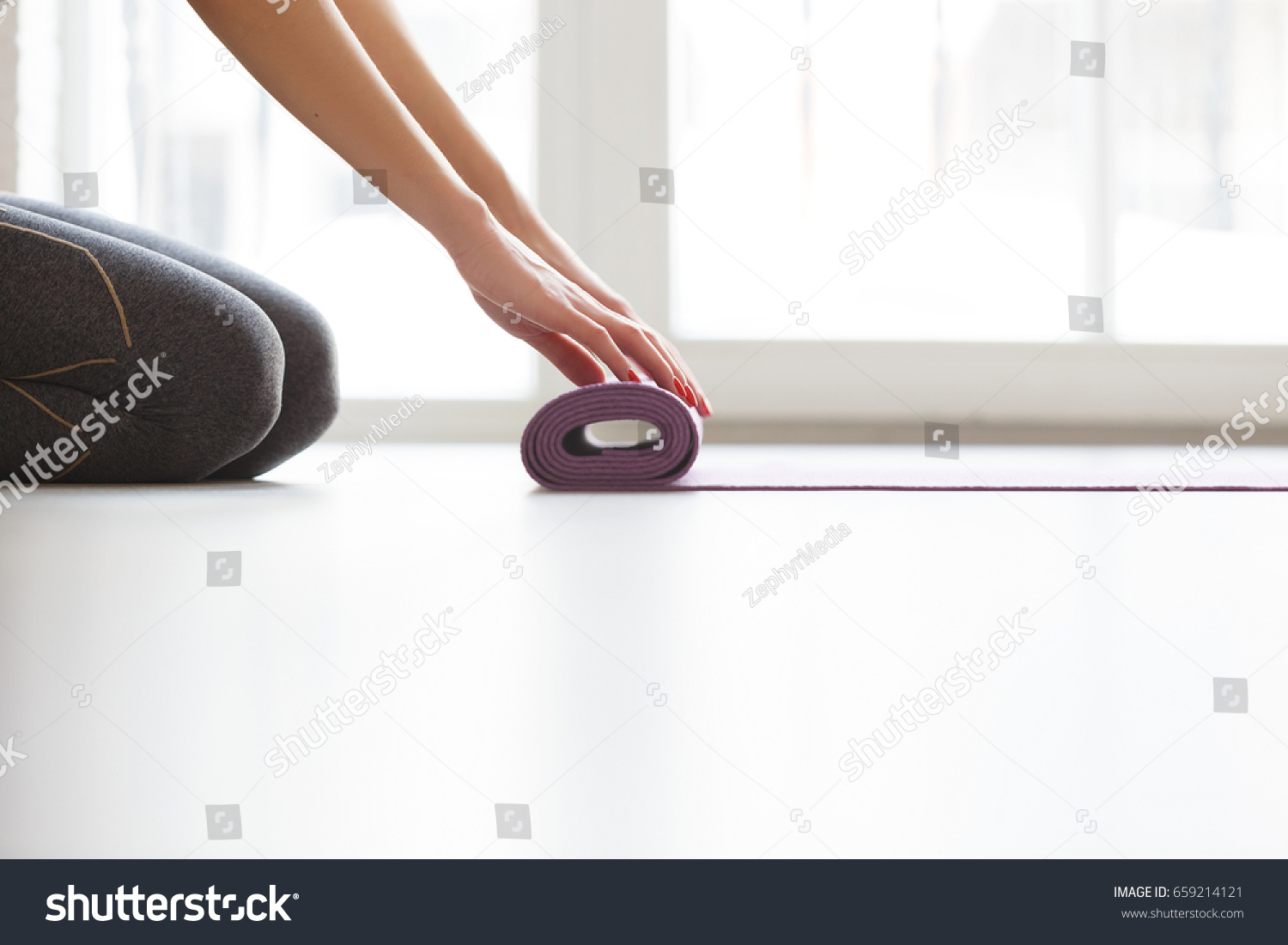 Young yoga Woman rolling her lilac mat after a yoga class on wooden floor near a window close up