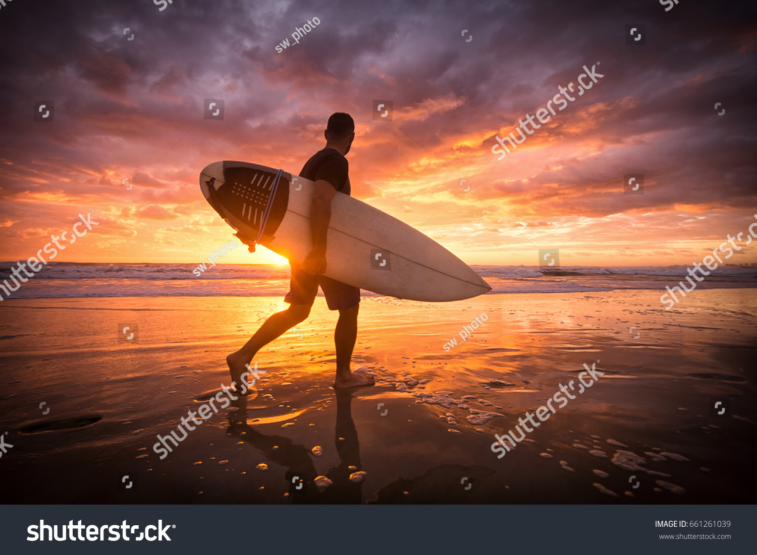 Surfer running on the beach at sunrise with reflections