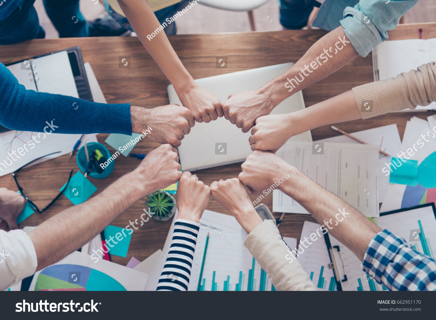Close up cropped photo of partners putting their fists together in a circle on top of the table with work stuff. Trust  friendship  unity  cooperation concept