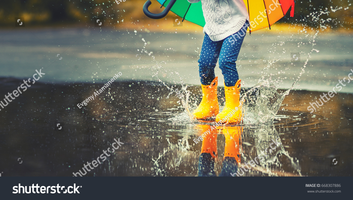 Feet of child in yellow rubber boots jumping over a puddle in the rain