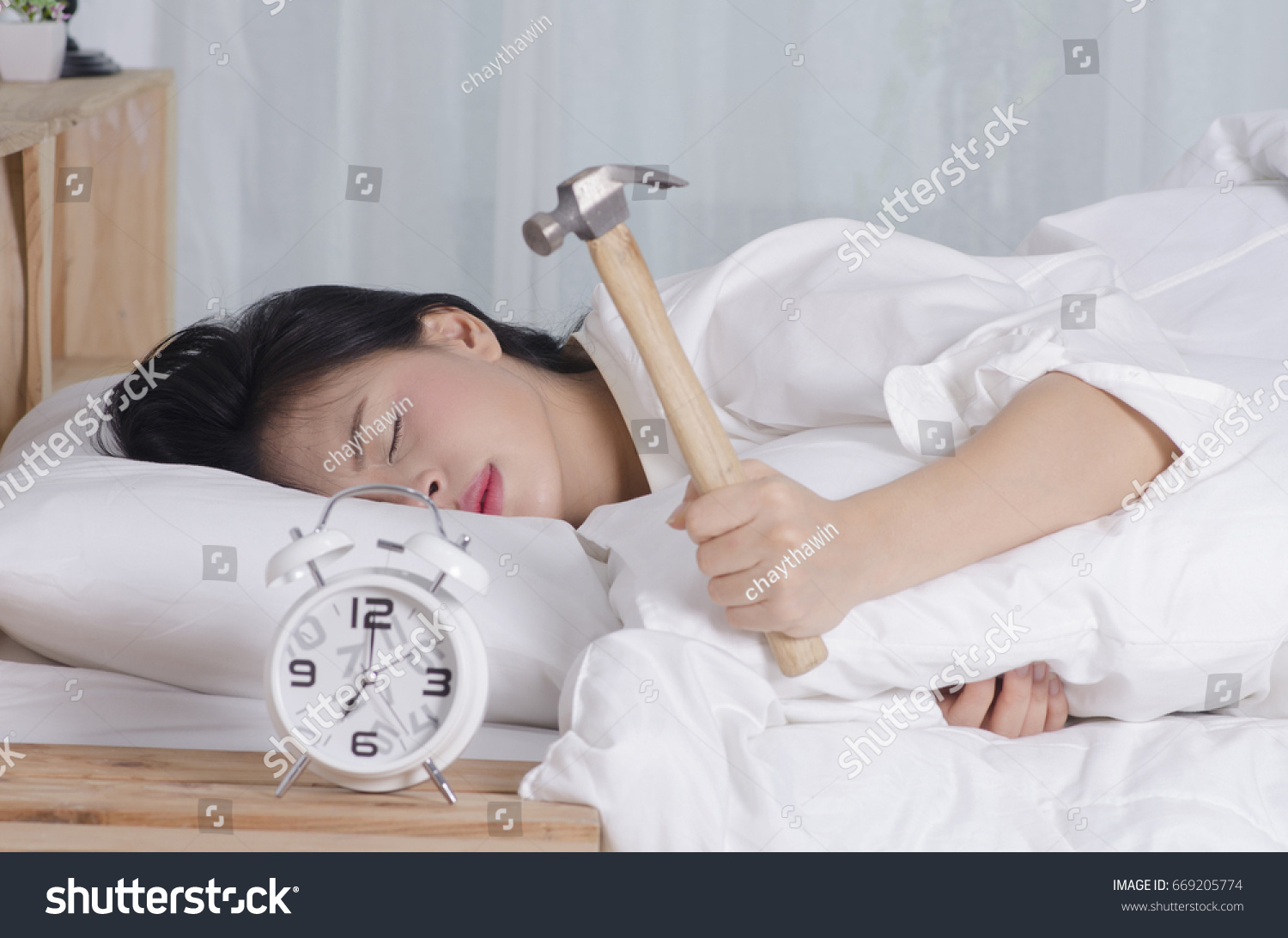 Beautiful young woman tries to break the alarm clock with hammer