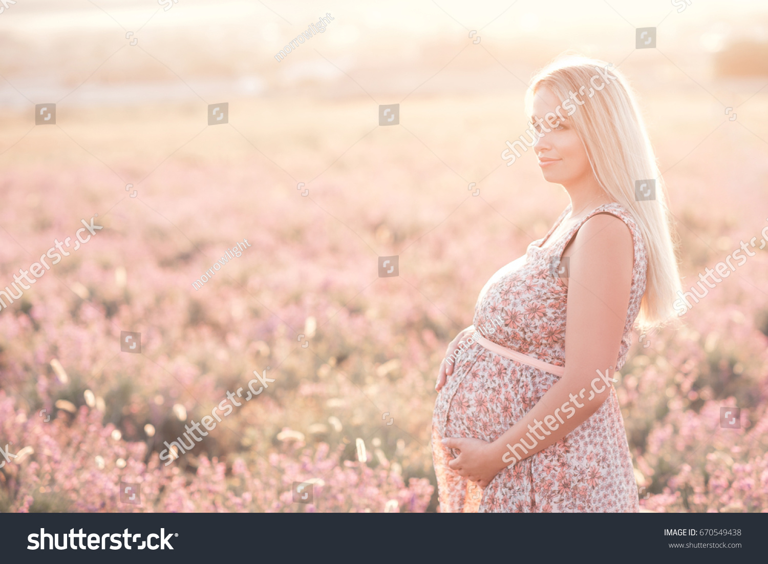 Smiling pregnant woman 25-29 year old resting in lavender field. Posing outdoors. Motherhood. Maternity. 20s.