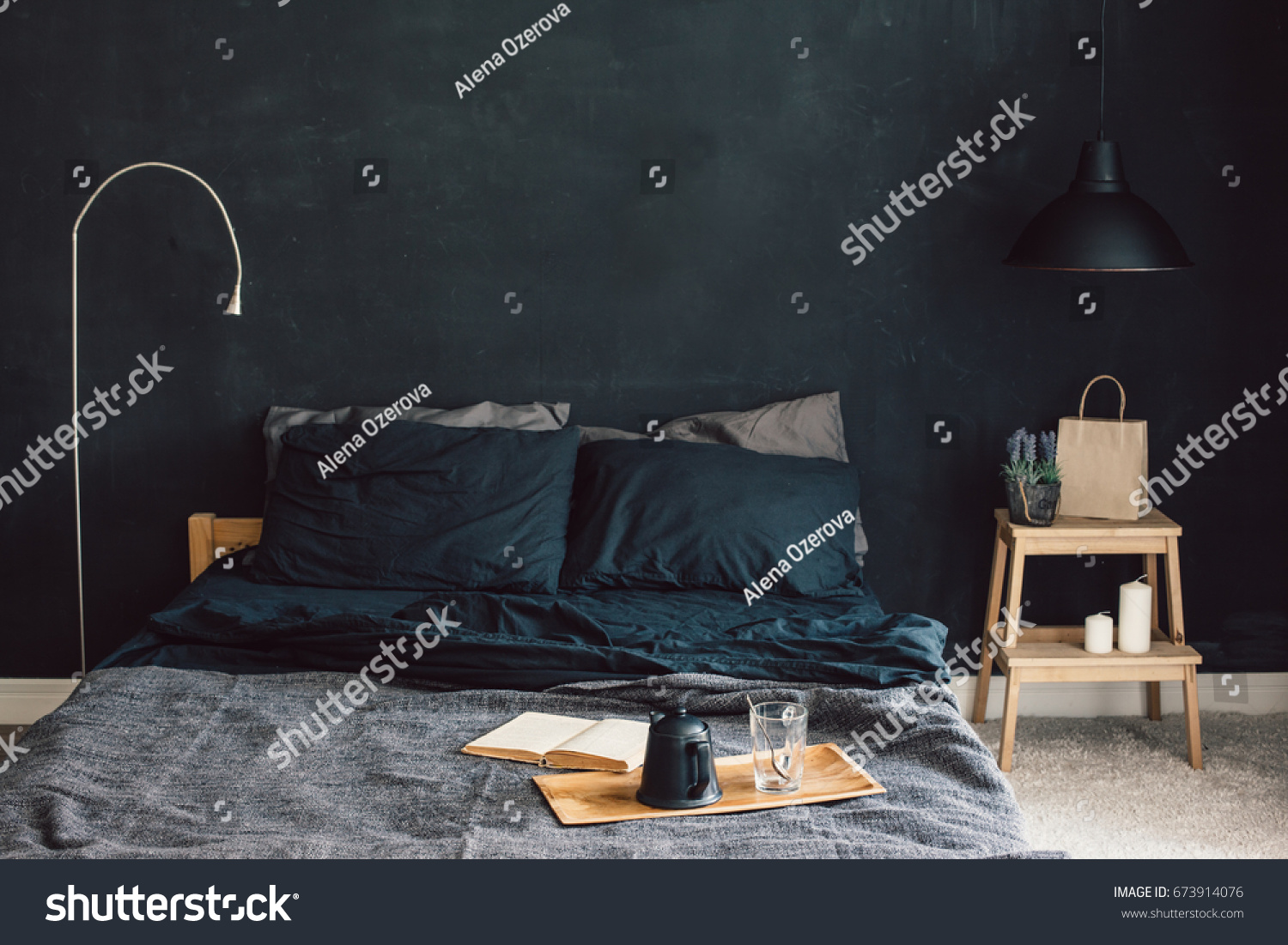 Black stylish loft bedroom. Unmade bed with breakfast and reading on tray. Lamp and interior decor over blank blackboard wall with copyspace. Cozy modern living space.