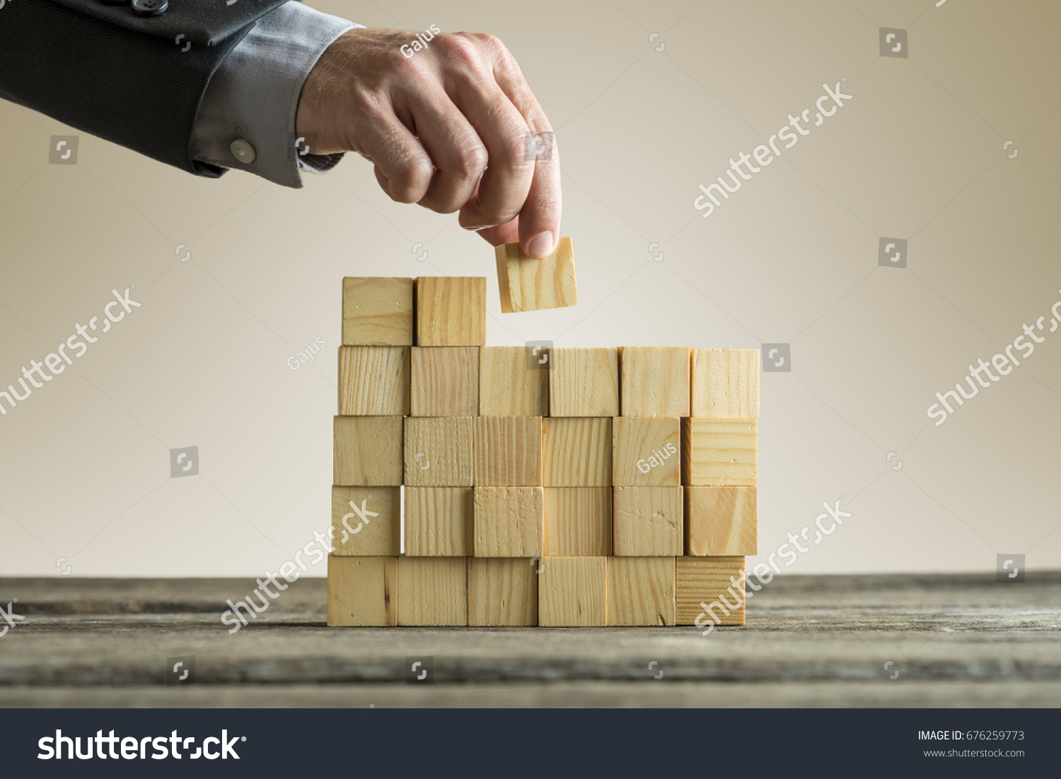 Businessman building a structure with wooden cubes on table surface on sepia toned background  concept with copy space.