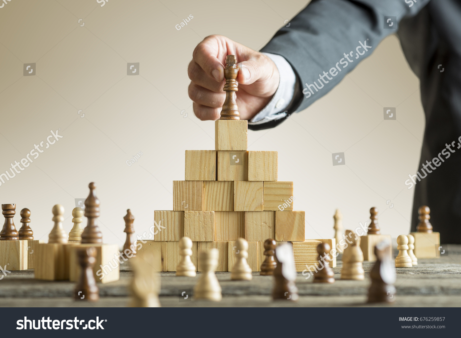 Businessman placing a chess piece on a pyramid of wooden building blocks in a concept of success and achievement in a close up view of his arm.